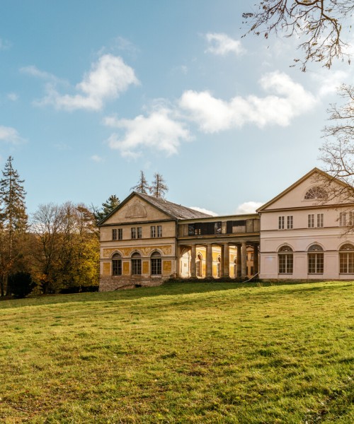 Schloss Wilhelmsthal bei Eisenach mit klassizistischer Fassade, umgeben von grüner Parklandschaft und herbstlichen Bäumen unter blauem Himmel.